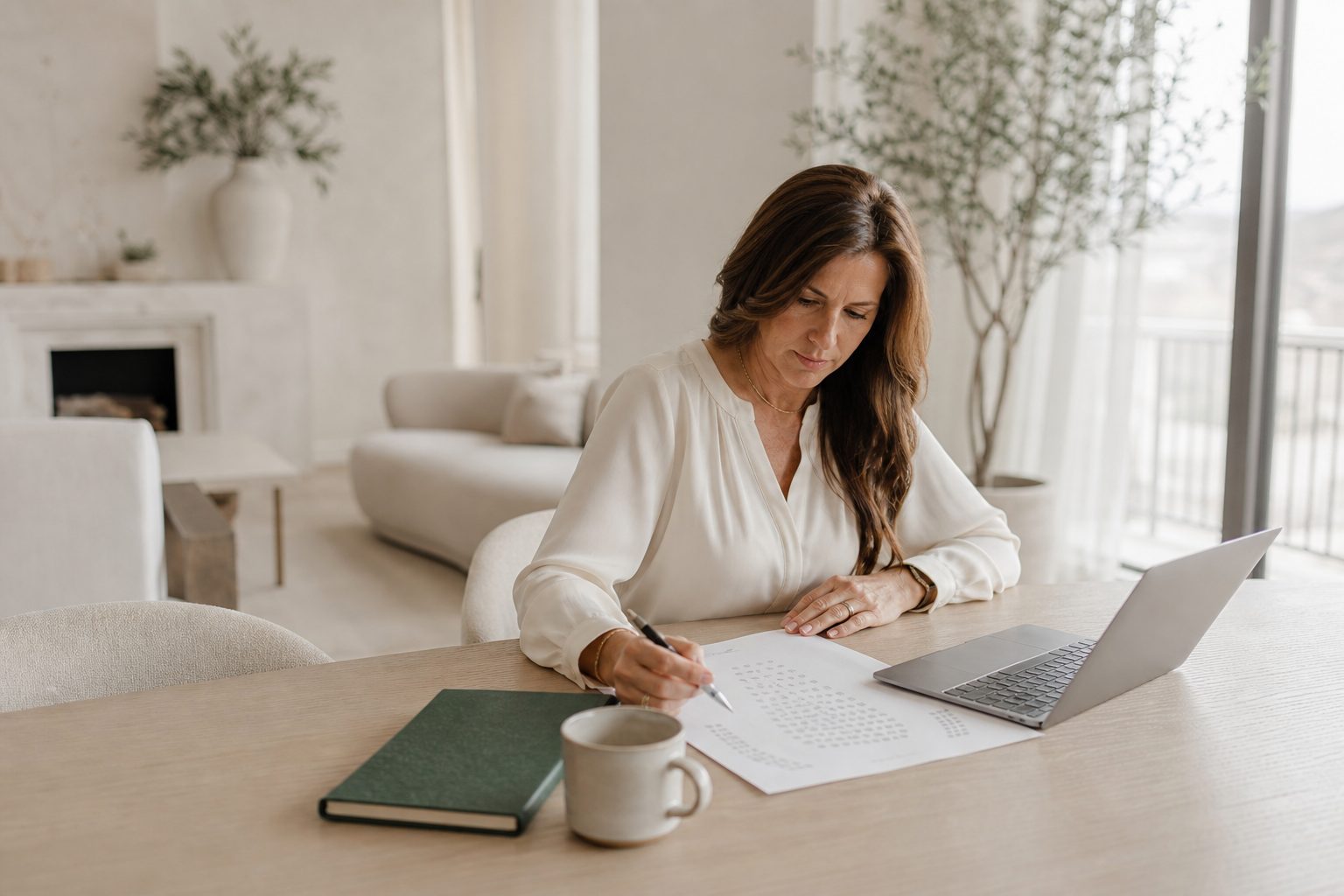 Coach working out mastermind seat pricing on a paper worksheet at a sunlit pale oak table